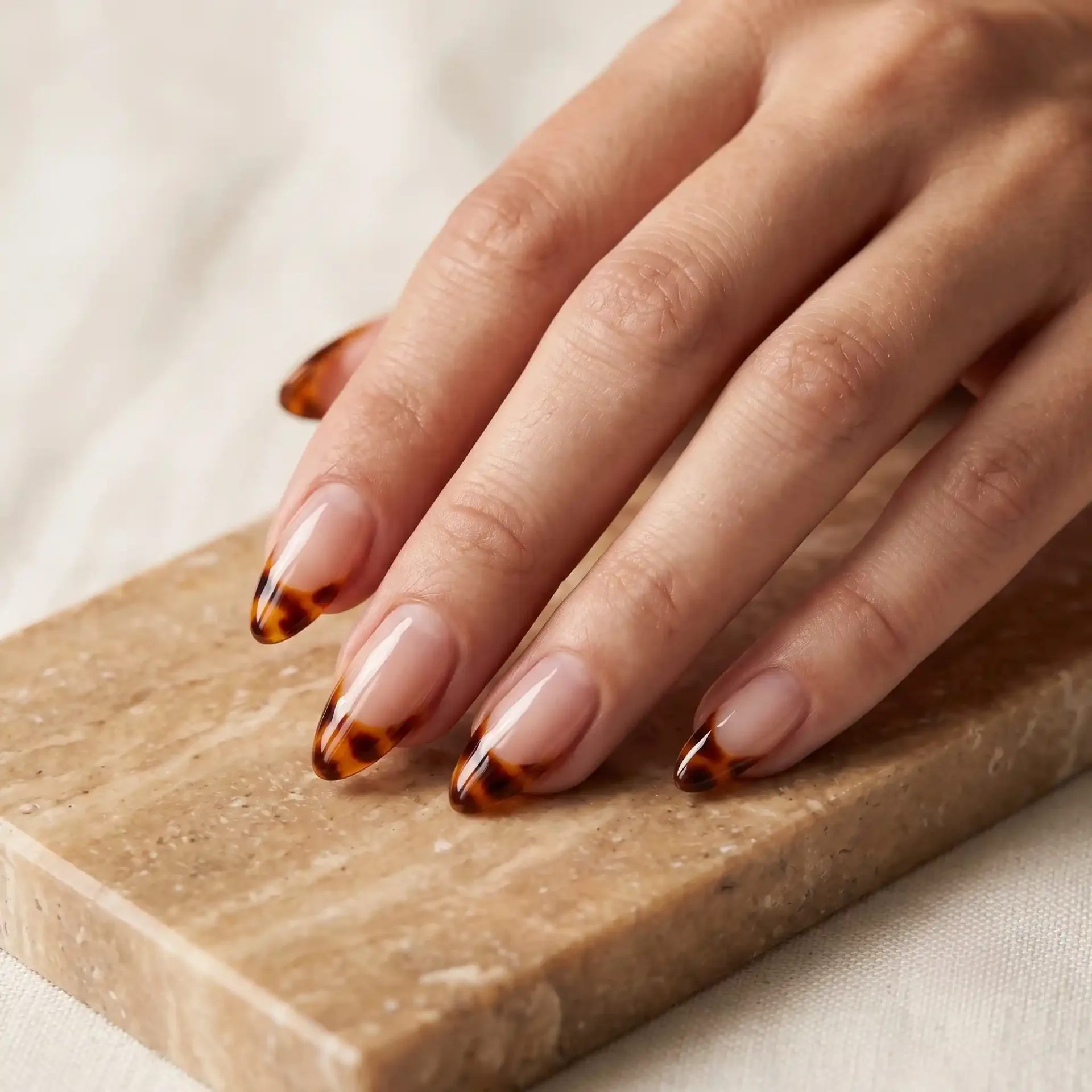 Closeup of high-gloss tortoiseshell French tip nails on almond shape.